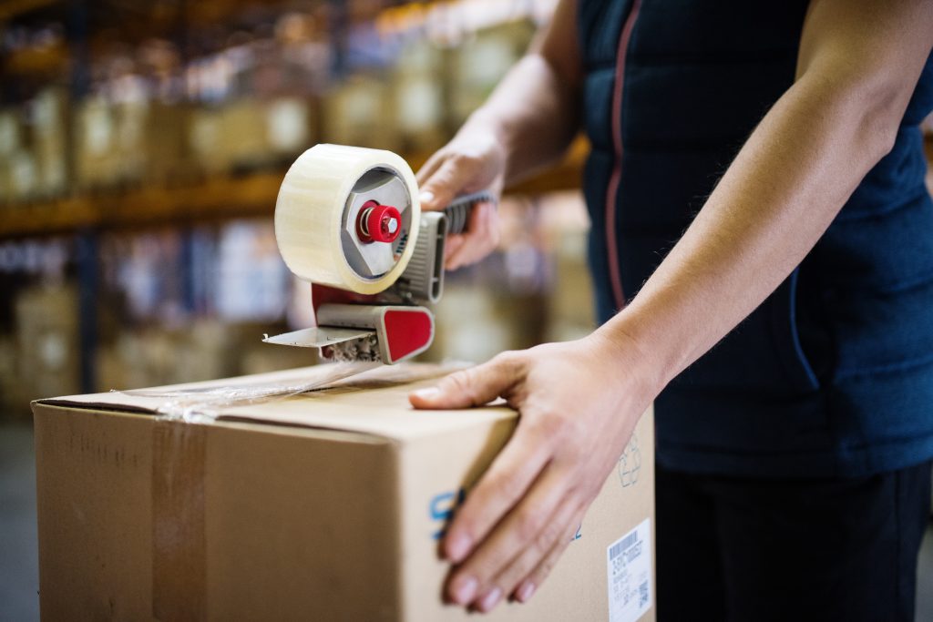 Unrecognizable male warehouse worker or a supercisor sealing cardboard boxes.