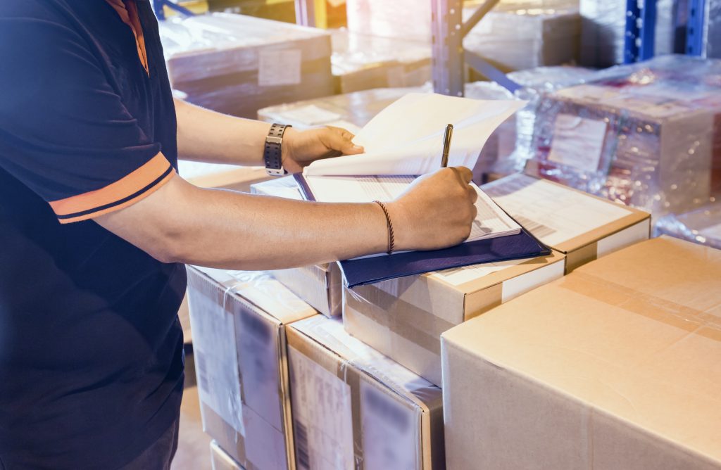 Warehouse worker writing on clipboard with checklist details shipments boxes, Warehouse inventory managemant.